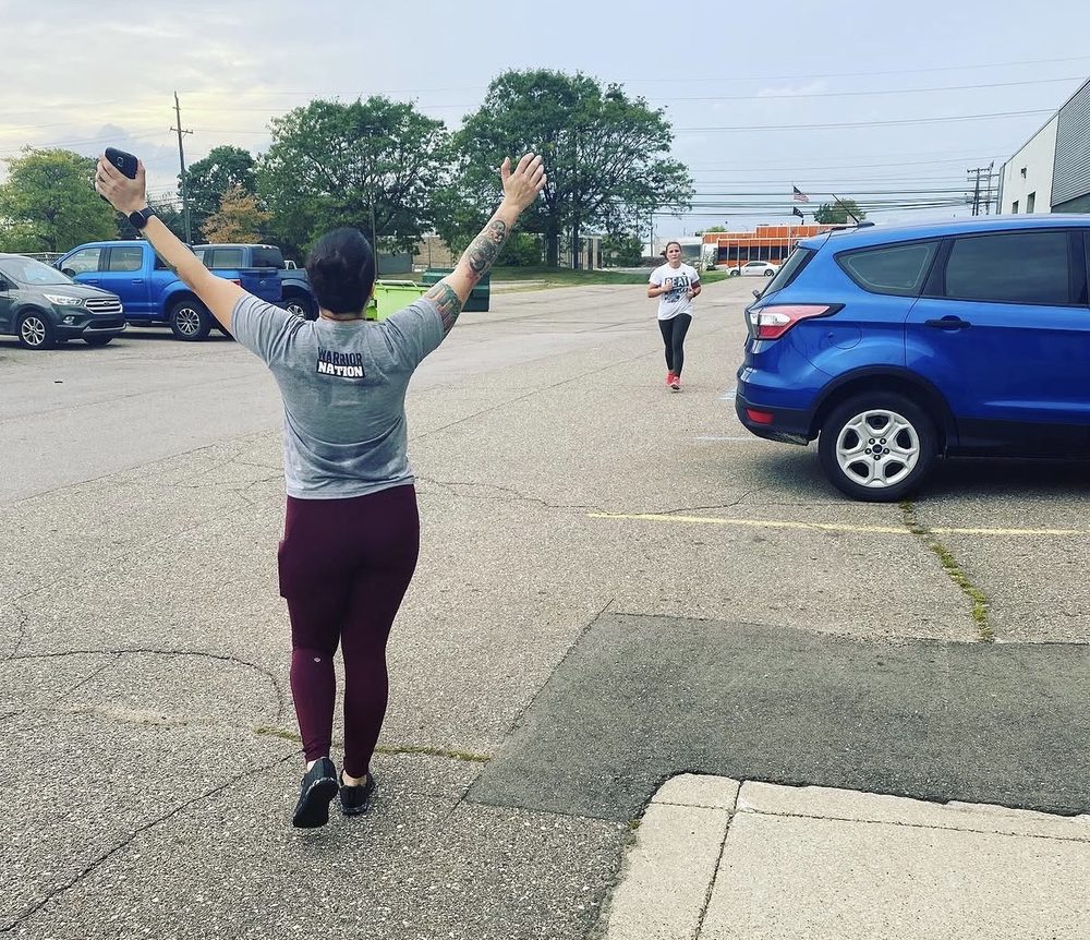 Jess coaching a client through a run in a parking lot, arms raised, calling out encouragement