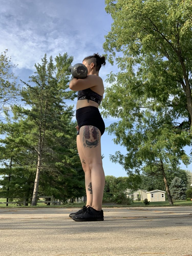 Jess standing tall holding a kettlebell in the front rack position outdoors