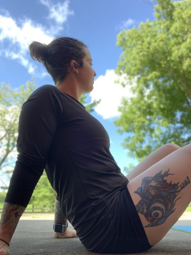 Jess sitting on the ground outdoors under a blue sky, resting between sets