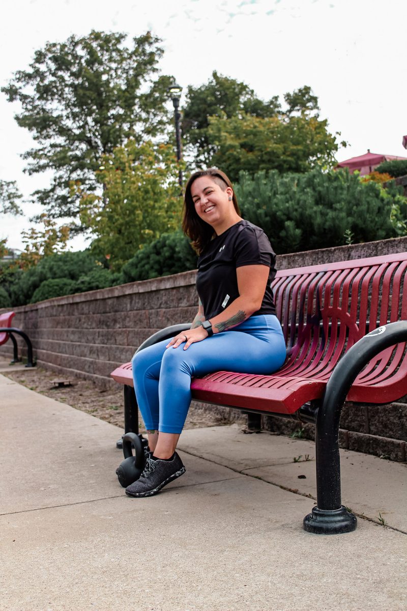 Jess sitting on a park bench beside a kettlebell, laughing