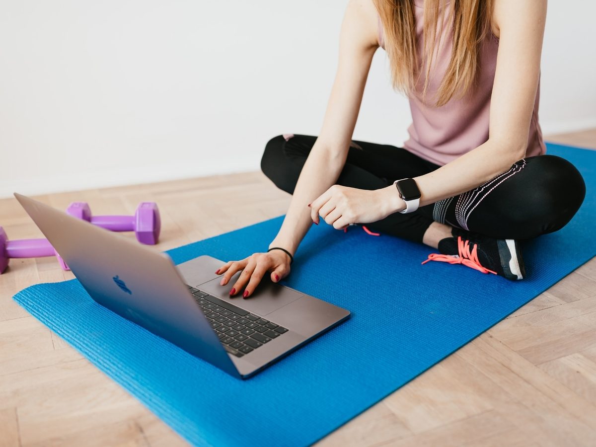 A client checks the week's programming on a laptop from her workout mat at home